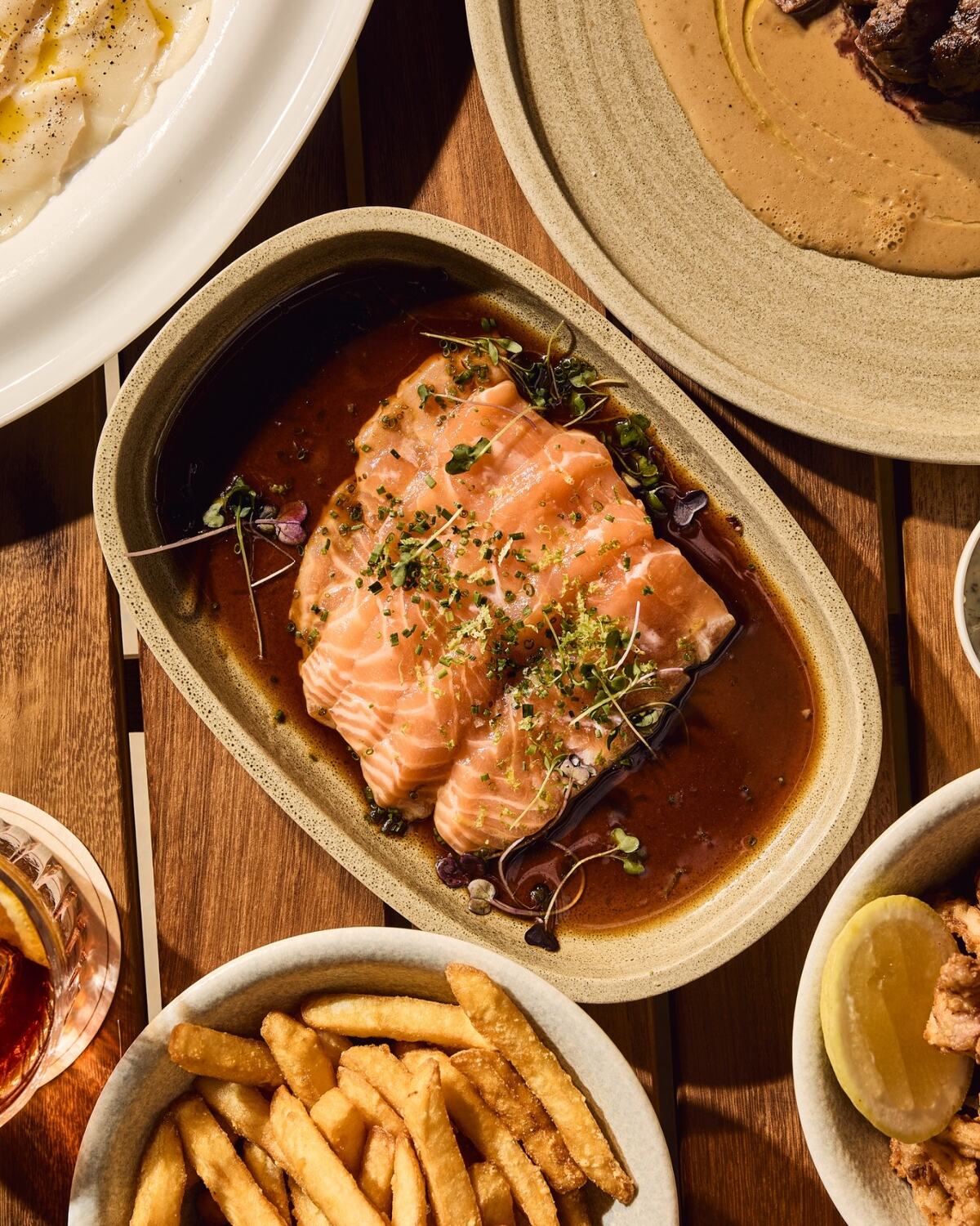 Soy-glazed salmon sashimi with chives and citrus zest, served with crispy fries.